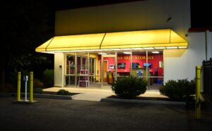 AA Self Storage office entrance at night in Lynchburg VA with bright yellow awning, red interior wall, and 